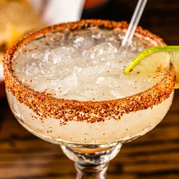 Close-up of a margarita with a chili-lime rim, ice, a straw, and a lime wedge.