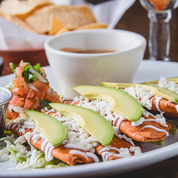 Mexican-style enchiladas topped with avocado, crumbly cheese, and crema, served with salsa, pico de gallo, chips, and coffee.