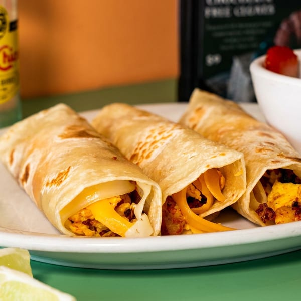 Three breakfast burritos with cheese and eggs, a side of fruit, and a Topo Chico.