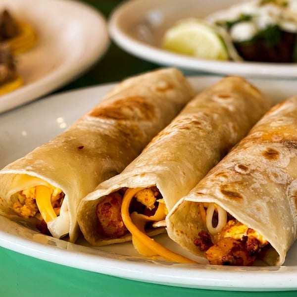 Three rolled burritos with cheese and meat, alongside a bowl of cherry tomatoes.