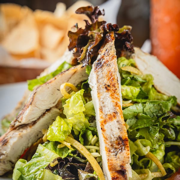 Grilled chicken strips atop a fresh lettuce salad with crispy tortilla strips and mixed greens on a white plate.