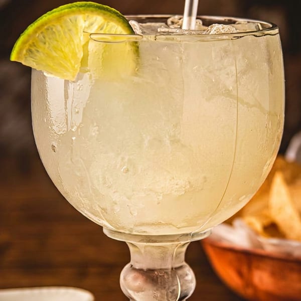 A frosty margarita with a lime wedge and straw, next to a basket of tortilla chips.
